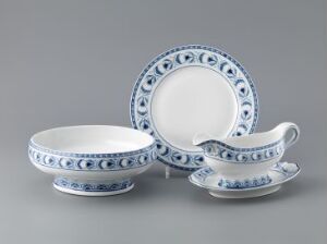  An exquisite set of white feldspar porcelain tableware with blue underglaze decoration, designed by Hans Flygenring, comprising a flat plate, a deep bowl, and a sauceboat, all displayed on a grey backdrop.