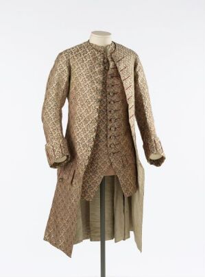  An historical men's coat with a beige and dark tan diamond patterned fabric, tailored with a fitted silhouette and split tails, displayed on a torso mannequin without any appendages.