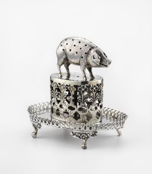  A detailed silver statuette of a speckled pig perched on an intricately designed cylindrical base with cut-out patterns, which is mounted on an ornate silver tray with scrolled edges and three small feet.