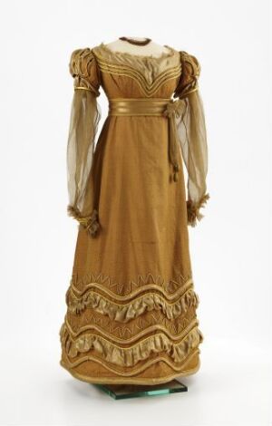  Vintage golden-brown dress with embroidered bodice and decorative scalloped hem, featuring sheer puffed sleeves and a cinched waist, displayed on a mannequin against a light background.