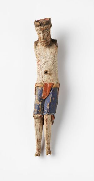  A vertically oriented, slender, carved wood figure, representing part of a crucifix by an unidentified artist. The figure, possibly made from birch, has a worn surface with traces of red and blue paint, and is titled "Del av krusifiks."