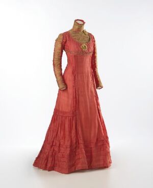  A long-sleeved red dress with sheer sleeves and a detailed neckline on a mannequin against a neutral background, highlighting the elegance and intricate textures of the fabric.