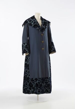  A vintage long-sleeved navy blue woman's coat with white fur collar and cuffs, featuring a double-row button closure and a floral pattern in lighter blue on the lower half, displayed on a mannequin against a light grey background.