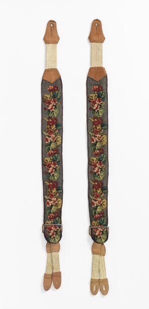  A set of ornate suspenders with a dark green background and vibrant red, green, yellow, and blue floral patterns, featuring tan leather accents and wooden and gold-toned fasteners at the ends.