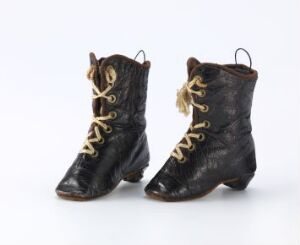  A vintage pair of black leather lace-up boots with tan laces against a light grey background, exhibiting signs of wear and a classic design reminiscent of Victorian style.