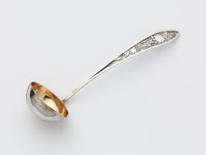  An elegant silver serving spoon with a gold-coated bowl and an intricately designed filigree handle, set against a light background.