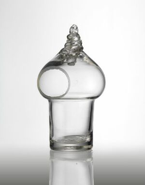  A clear glass decorative bottle with a cylindrical base and an ornate loop forming the neck, capped with a glass droplet decoration, against a graduated grey to white background.