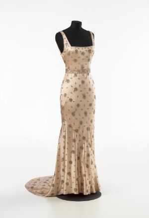  An elegant champagne beige evening gown with coffee brown polka dots fitted on a headless and armless mannequin with a black upper part, standing against a light grey background.