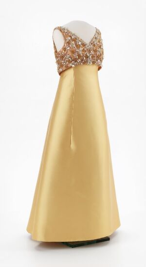  An elegant, gold-colored floor-length dress with a fitted bodice densely adorned with gold sequins or beads, creating a sweetheart neckline over a sheer upper chest area, flaring out into a satiny, smooth skirt.