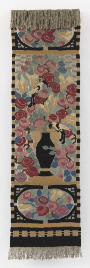  An antique vertical textile bookmark or wall hanging with intricate floral and foliage embroidery in shades of pink, green, and navy, featuring a central circular motif with a figure dressed in black, set against an off-white background