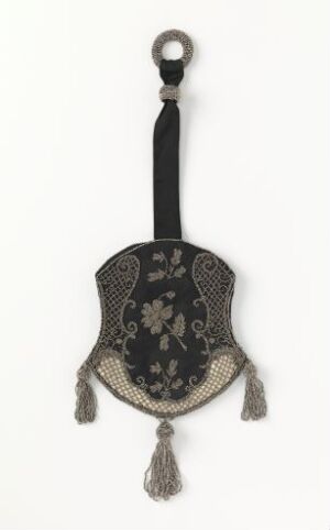  An ornate inverted teardrop-shaped object with a circular metal handle, detailed with symmetrical light-colored embroidery on a black background, and featuring three tassels at the bottom.