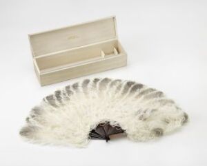  A vintage off-white feathered hand fan partially opened, displaying light gray accents at the feather tips, set beside its simple cream-colored box on a neutral light gray background.