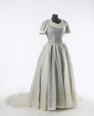  A vintage-inspired dress with short sleeves and a round neckline, featuring a contrasting bodice in light grey or off-white, and a full, bell-shaped skirt in soft white or pale ivory, displayed on a mannequin against a neutral background. Artist name and title are unknown.