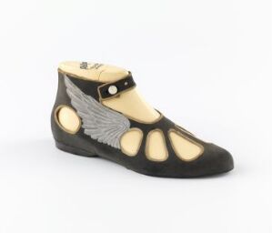  A PVC costume shoe by Phillips Shoes, black with grey and white winged design on the sides and beige toe outlines, featuring a light tan ankle strap with a buckle.